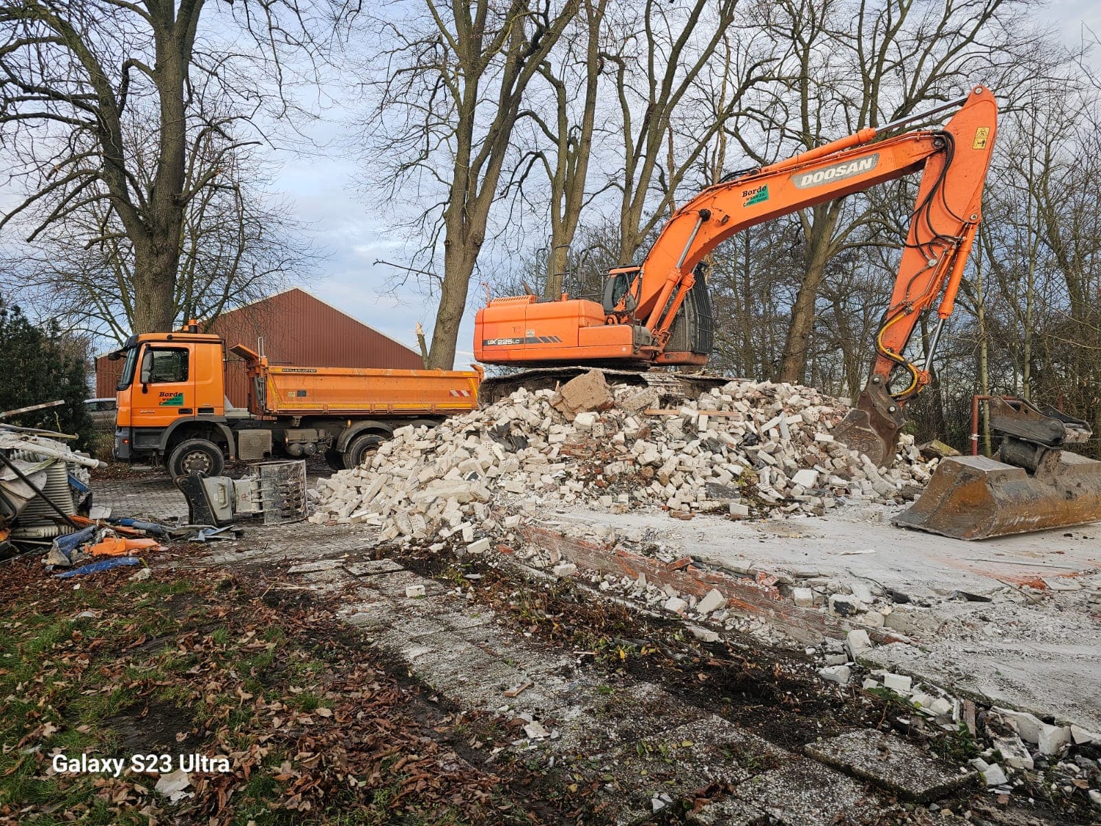Bagger sortiert Bauschutt auf einem Abbruch-Grundstück, Kipplaster von Landschaftpflege Borde im Hintergrund.