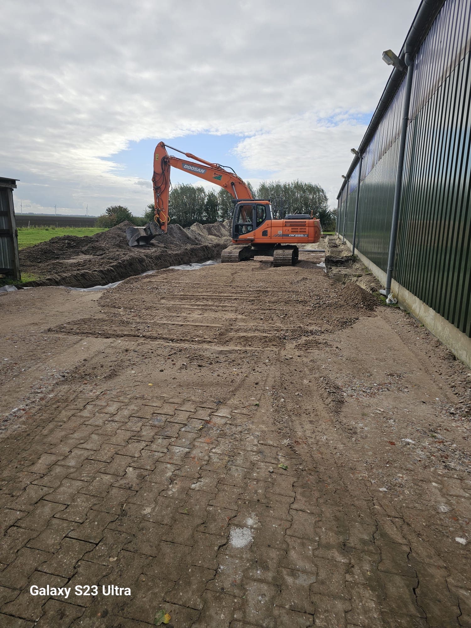 Doosan-Bagger von Landschaftpflege Borde arbeitet auf einer befestigten Fläche direkt neben einer Halle.