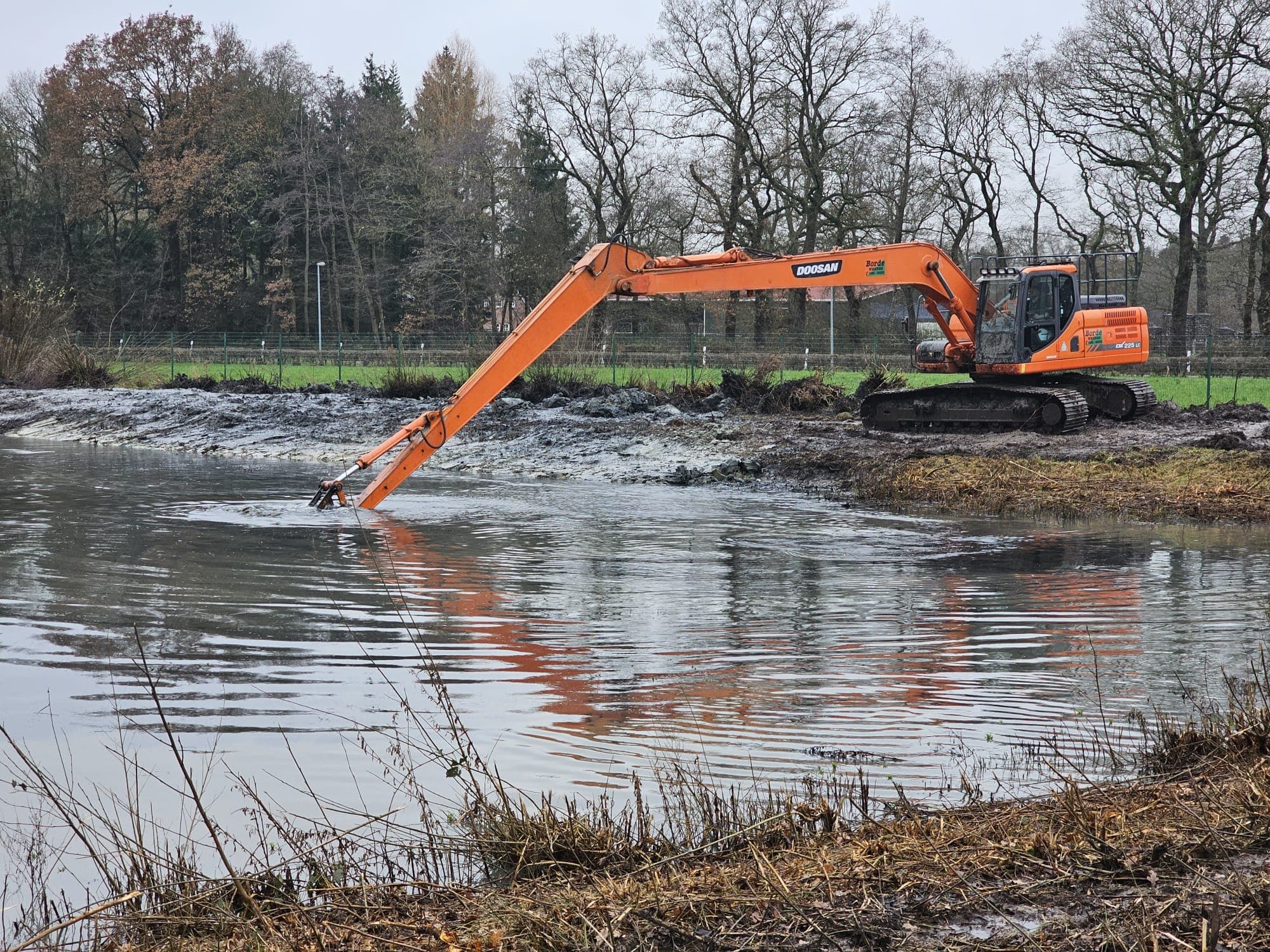 Langarmbagger bei der Grabenreinigung direkt im Wasser, mit Spiegelung.